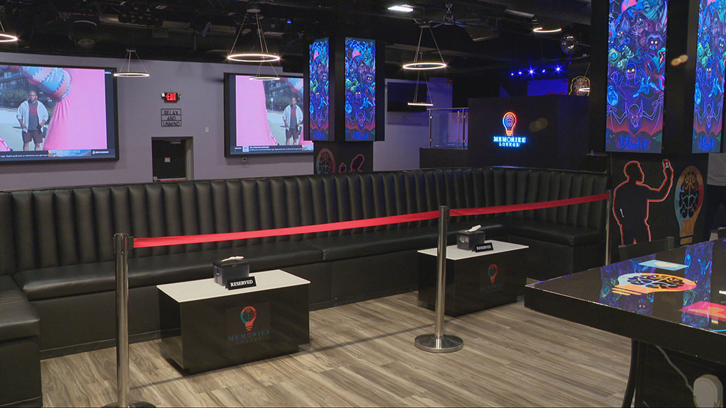 The inside of Memories Lounge, a sleek, cozy hangout spot. There are a few TVs hanging on the walls, and the lounge is decorated with colorful neon art and illustrations.